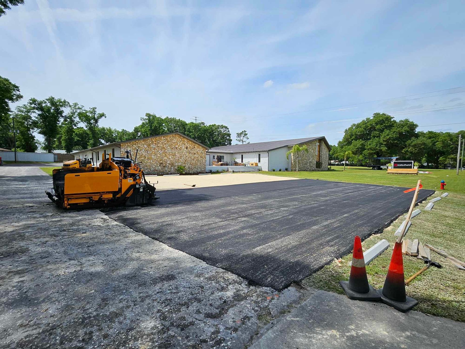 A yellow tractor is laying asphalt in a parking lot