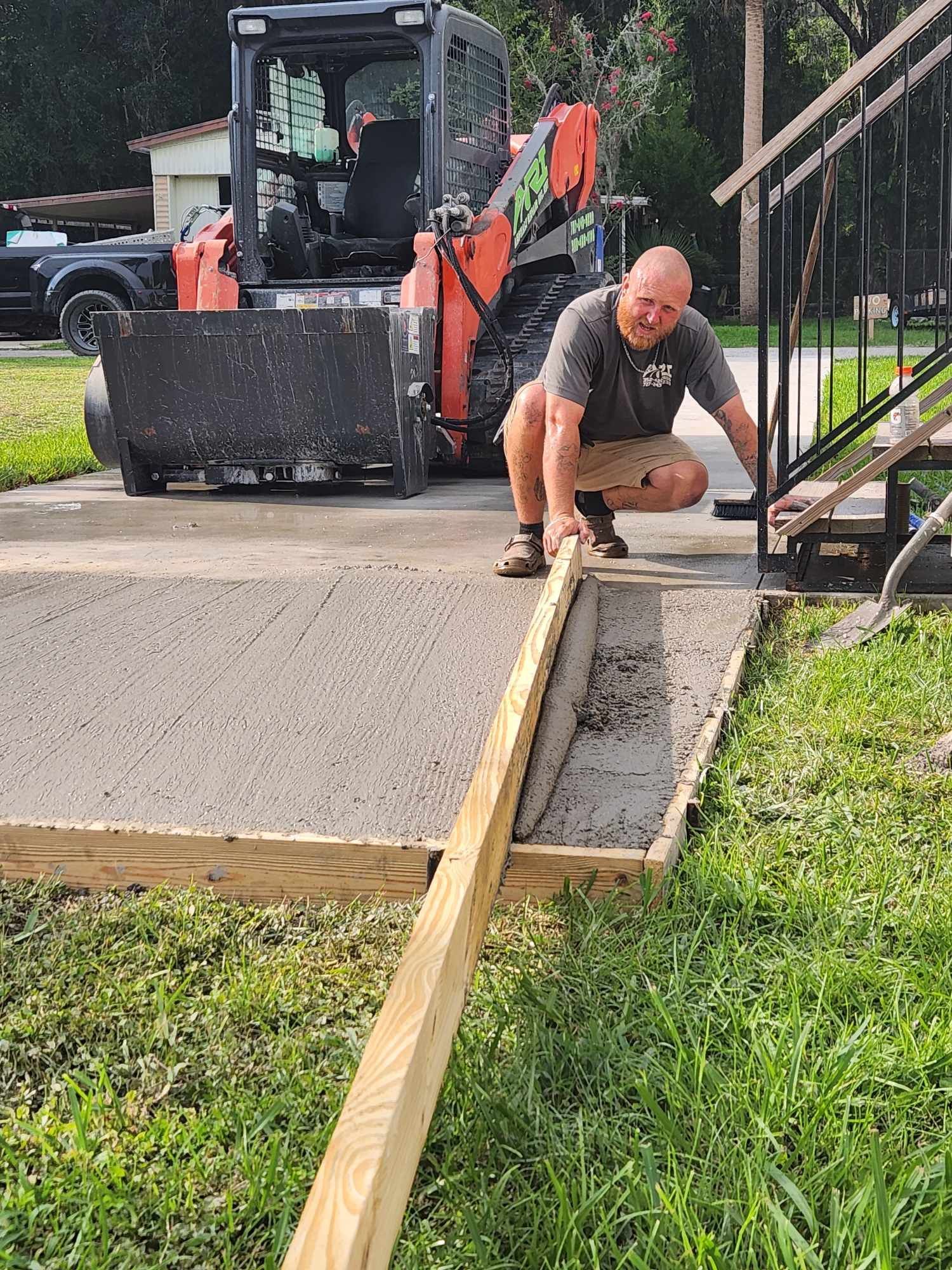 A man is kneeling next to a wooden plank in front of a bulldozer