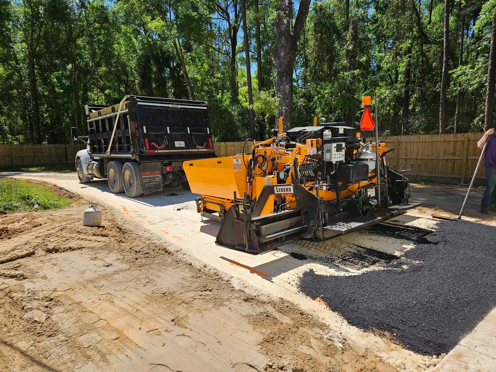 A tractor is laying asphalt on a dirt 