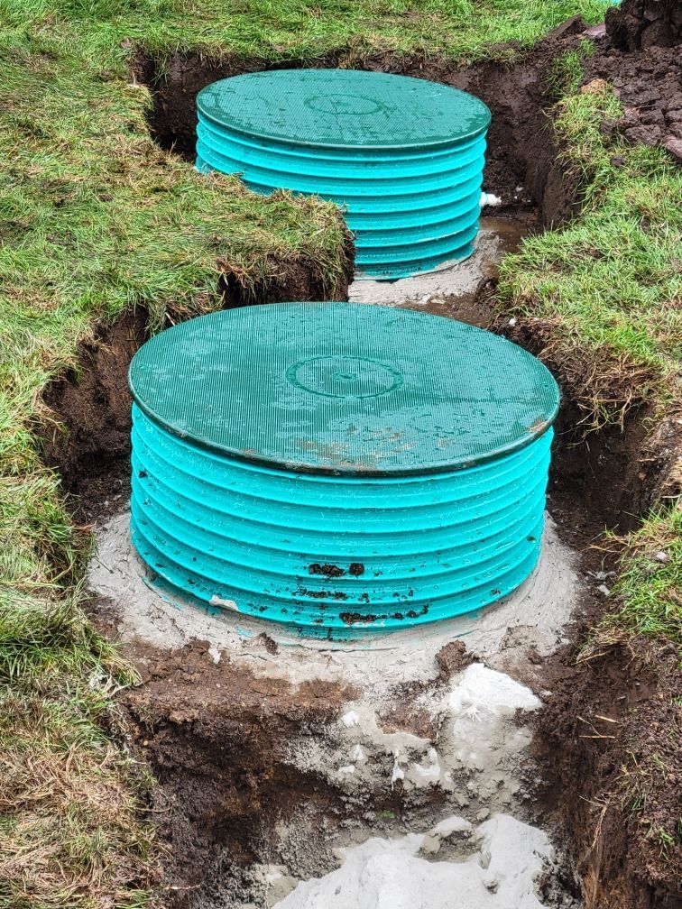 Two turquoise septic tanks installed in excavated ground, with concrete bases.