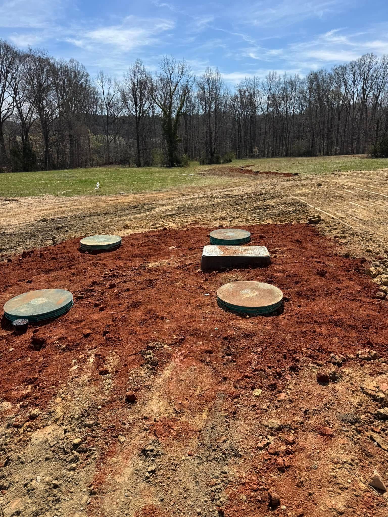 Five septic system covers in red soil in a grassy field under a blue sky.