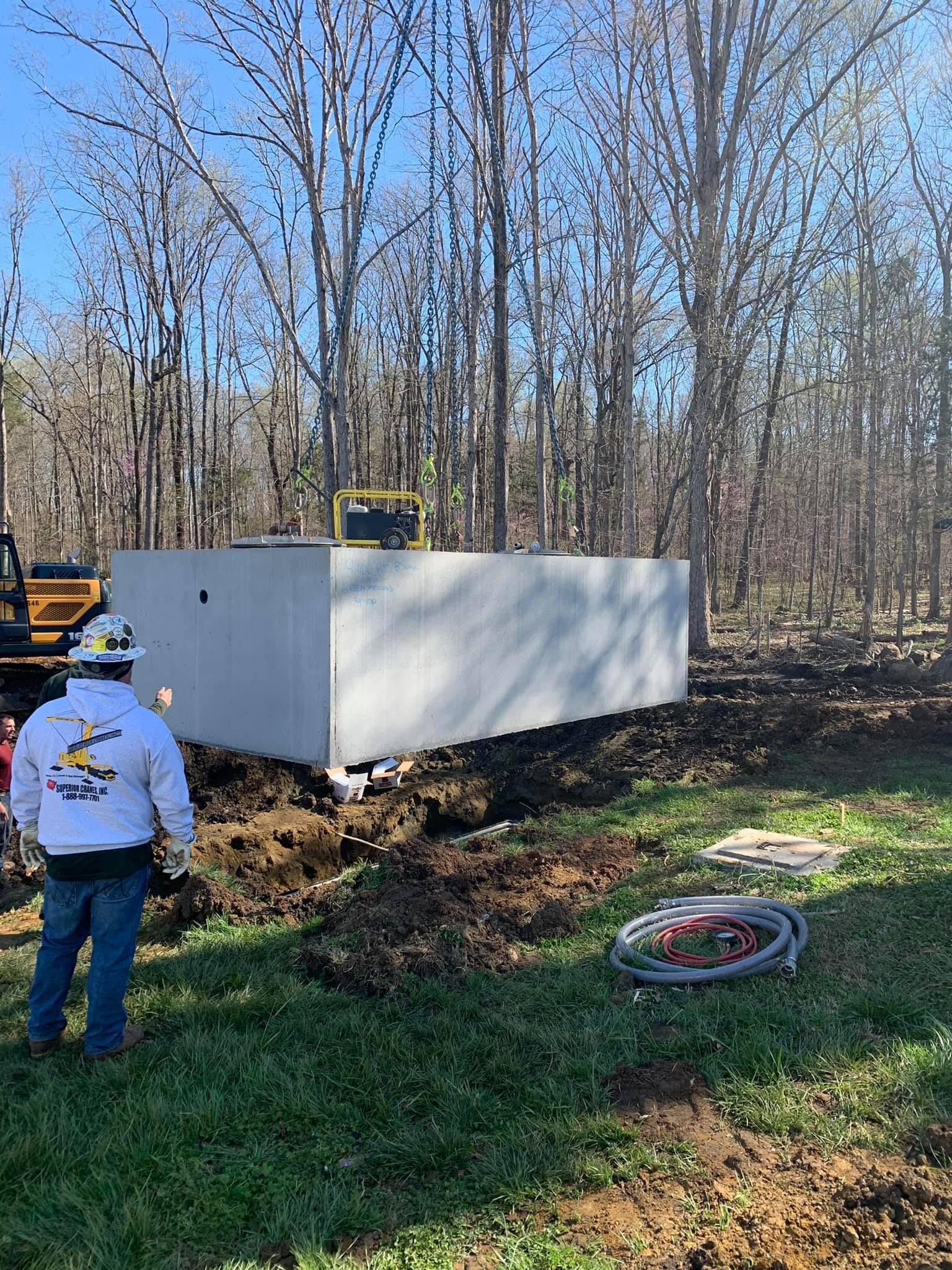 Construction worker surveys a large concrete structure in a wooded area. Equipment visible.