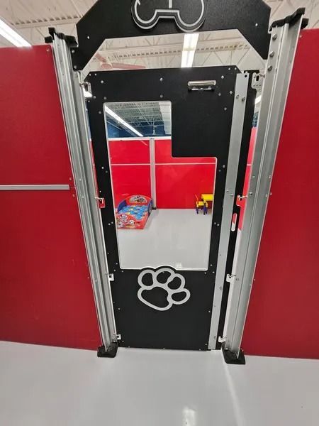 Dog-themed doorway with a paw print cutout, black door, and clear window, in a red-walled space.
