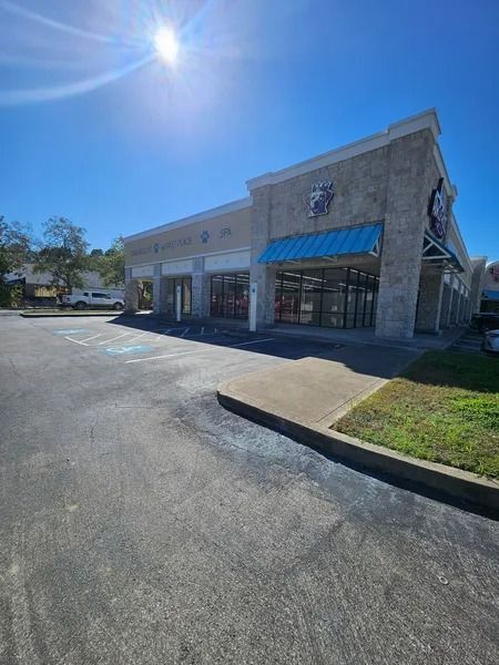 Exterior of a commercial building with a blue awning and open glass windows. Sunny day.