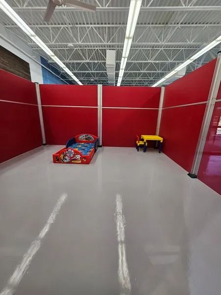 Red walled area with a child's bed and table set inside. White floor and ceiling.