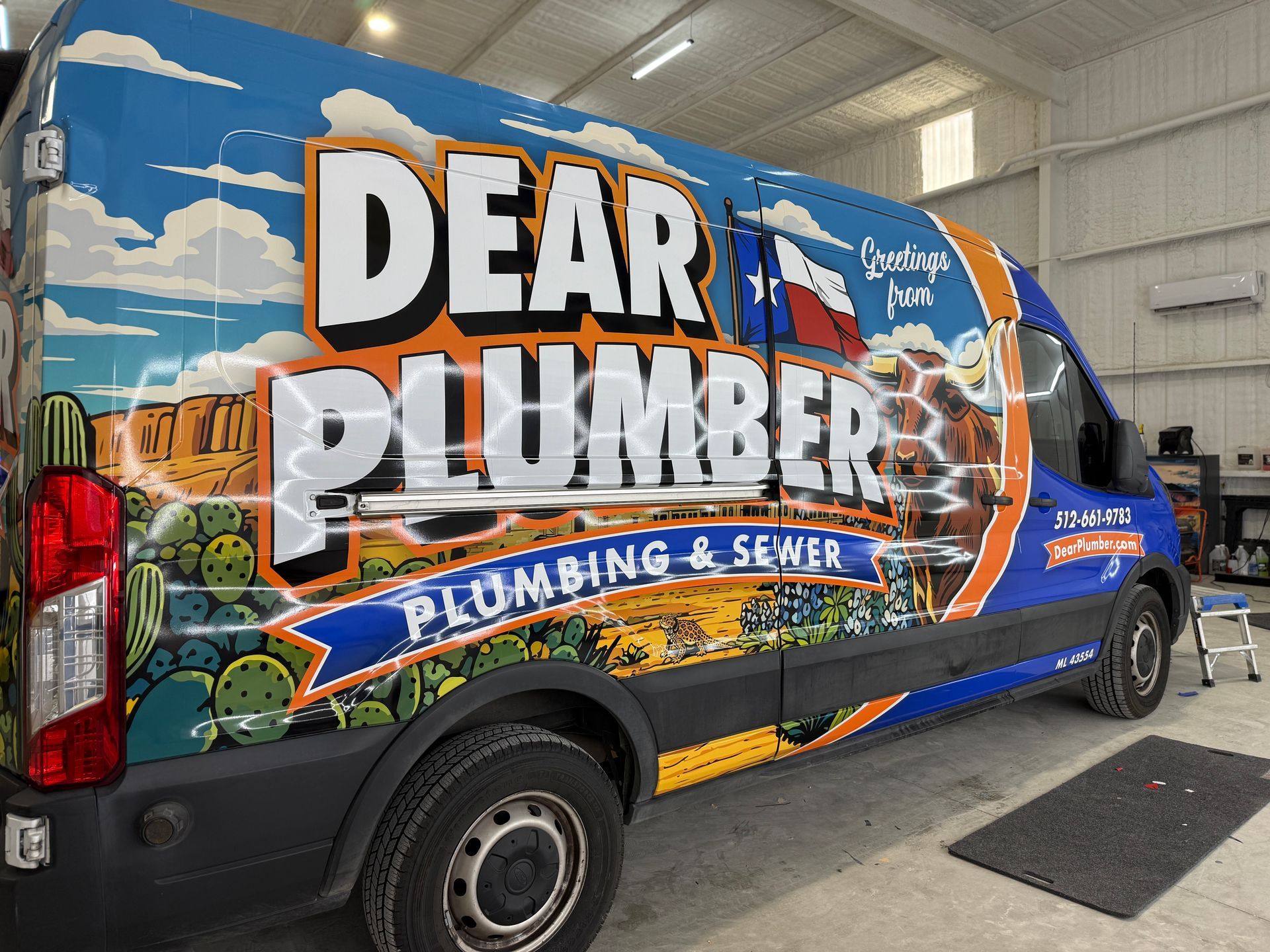Blue Dear Plumber service van with large plumbing and sewer graphics parked indoors