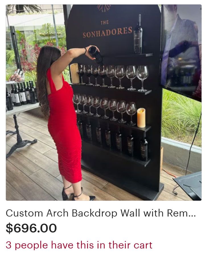 Woman in red dress reaching for wine bottle at wine display wall.