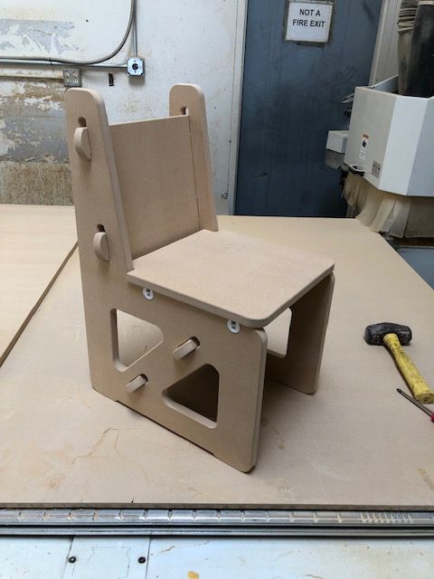 A small wooden chair is sitting on a table next to a hammer