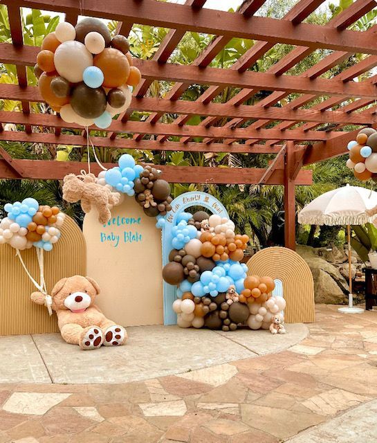 A teddy bear is sitting in front of a wall decorated with balloons