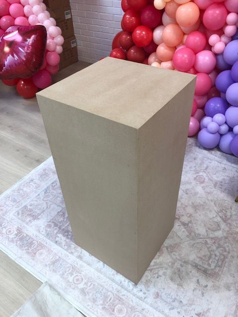 A wooden cube is sitting on a rug in front of balloons