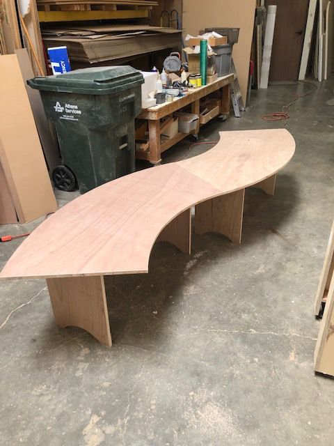 A wooden bench is sitting in a room next to a trash can