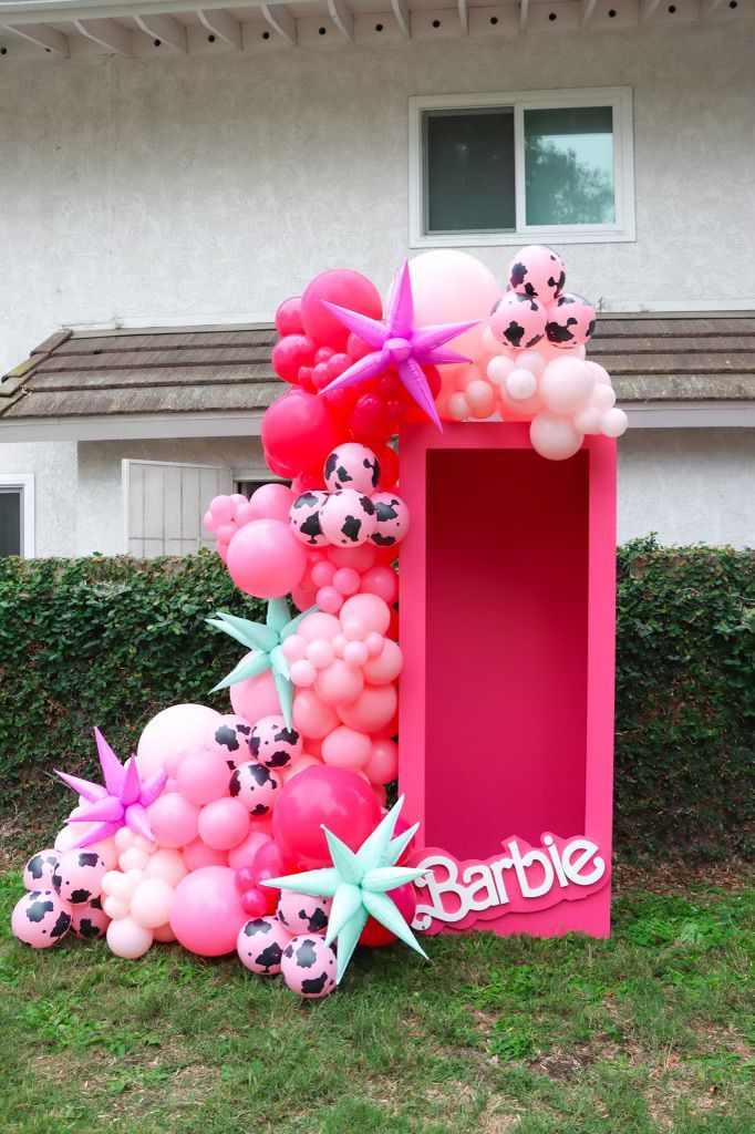 A pink box filled with balloons and a sign that says barbie is sitting in the grass in front of a house