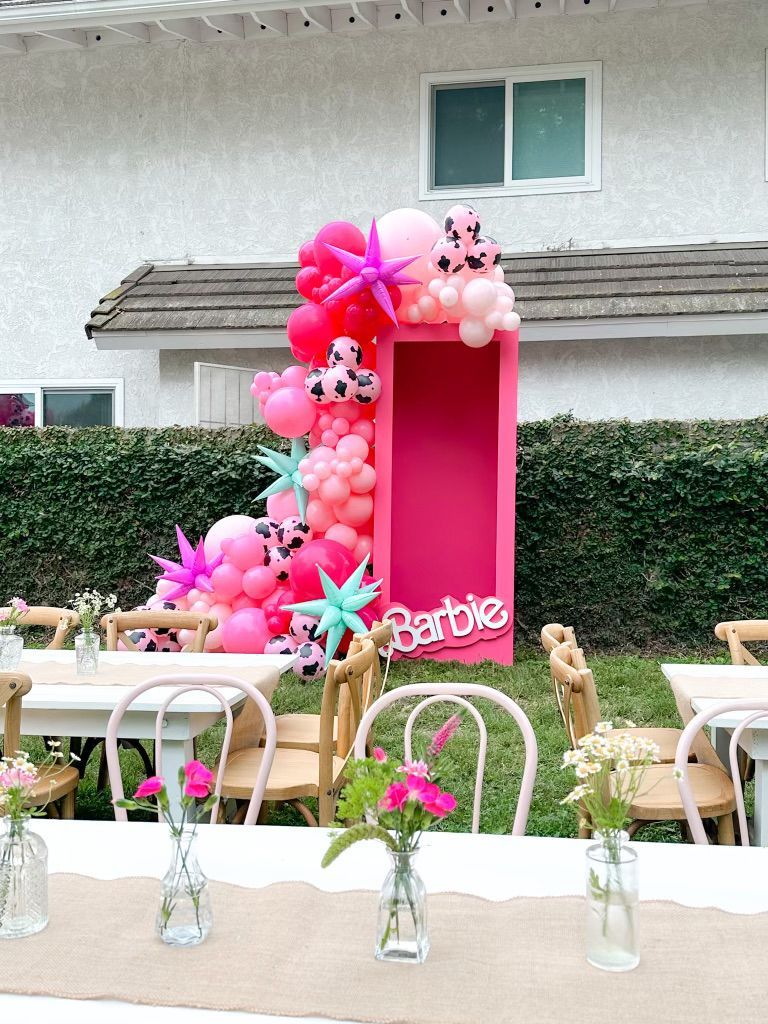 A barbie doll box is decorated with balloons and flowers for a birthday party