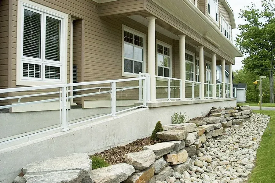 Exterior of building with white railing, ramp, windows, and stone retaining wall.