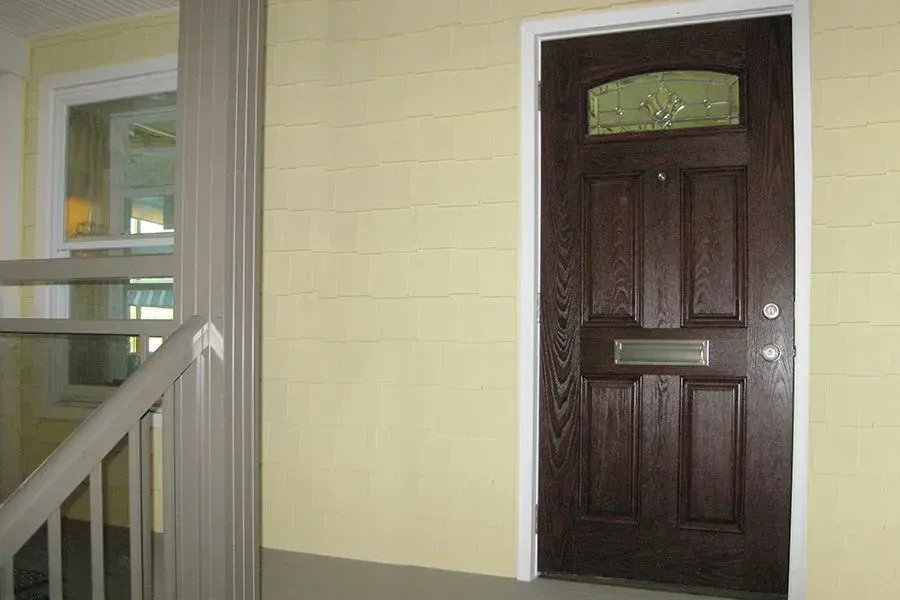 Dark wood front door with stained glass, next to a window and staircase. Yellow walls.