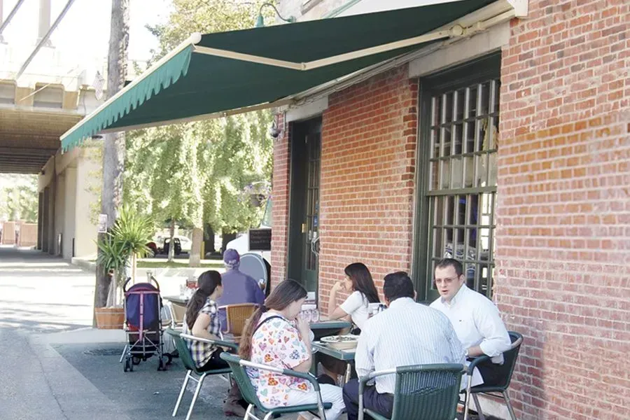 People seated at outdoor cafe tables under a green awning, against a red brick building.