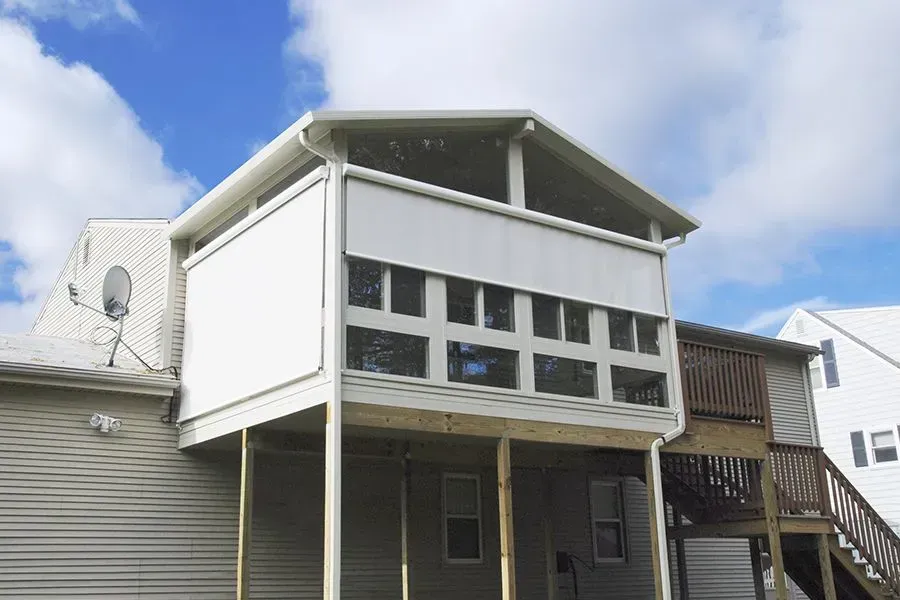 White porch with windows and screened enclosure on a wood deck against a blue sky.