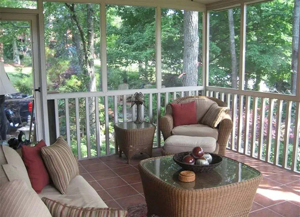 Screened porch with wicker furniture and view of trees.