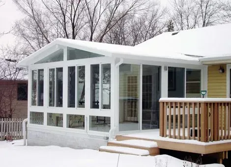 Sunroom with large windows and a white frame attached to a house with snow on the ground.