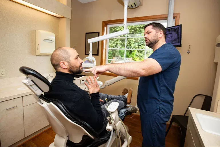 A man is sitting in a dental chair talking to a dentist.