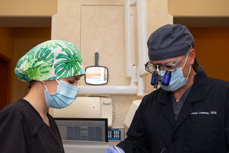 A dentist and a nurse wearing masks and glasses are working on a patient 's teeth.