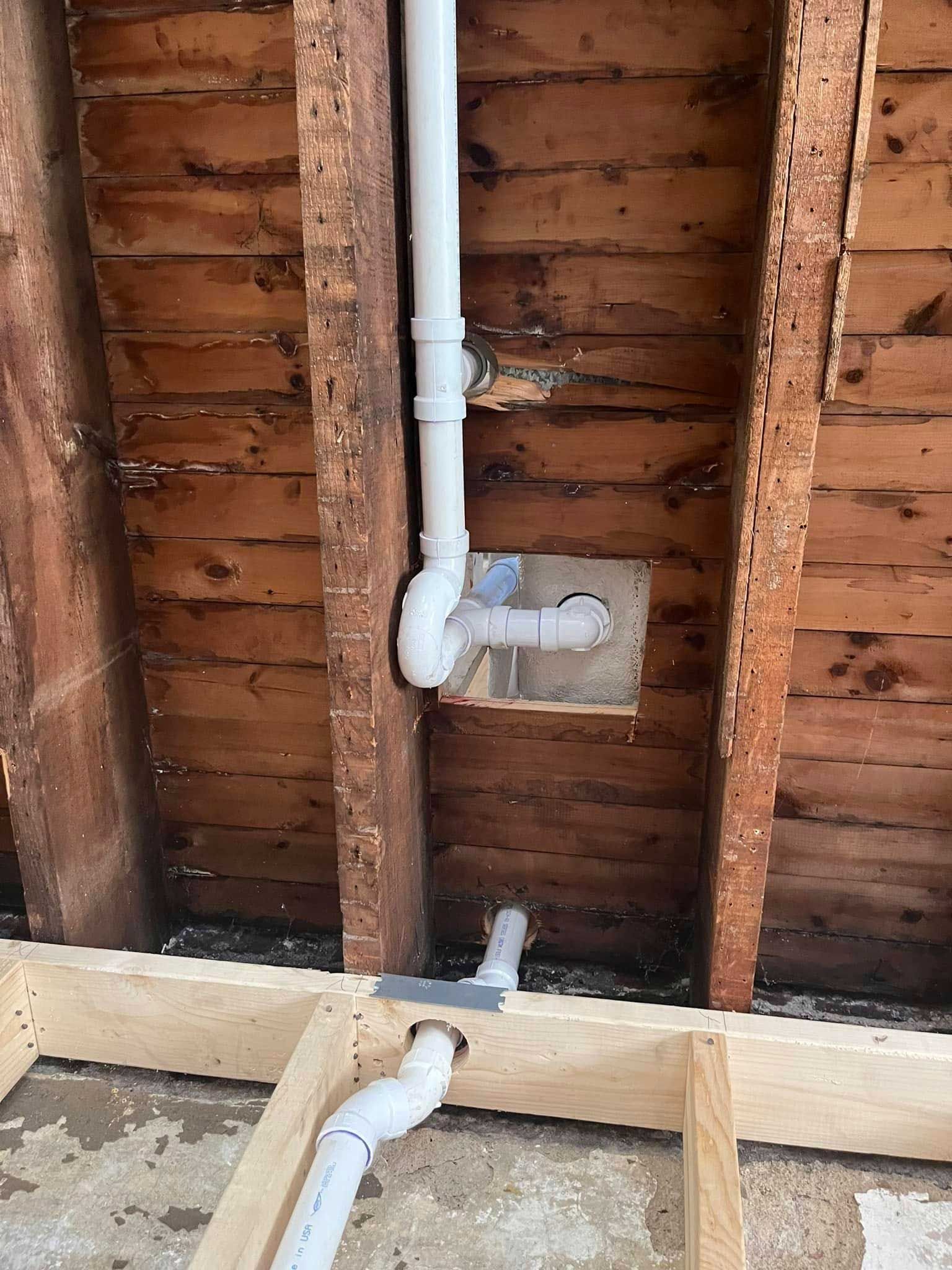 Plumbing pipes running through a wooden frame in a wall. White pipes contrast with the brown wood.