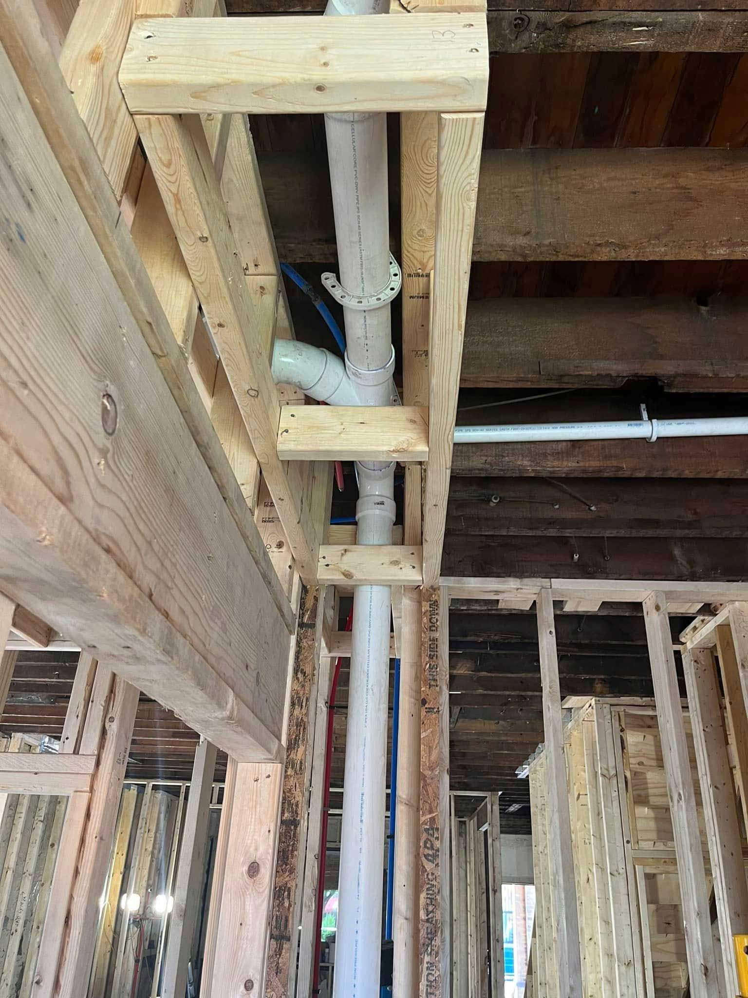 White plumbing pipes installed within wooden framing of a building's structure.