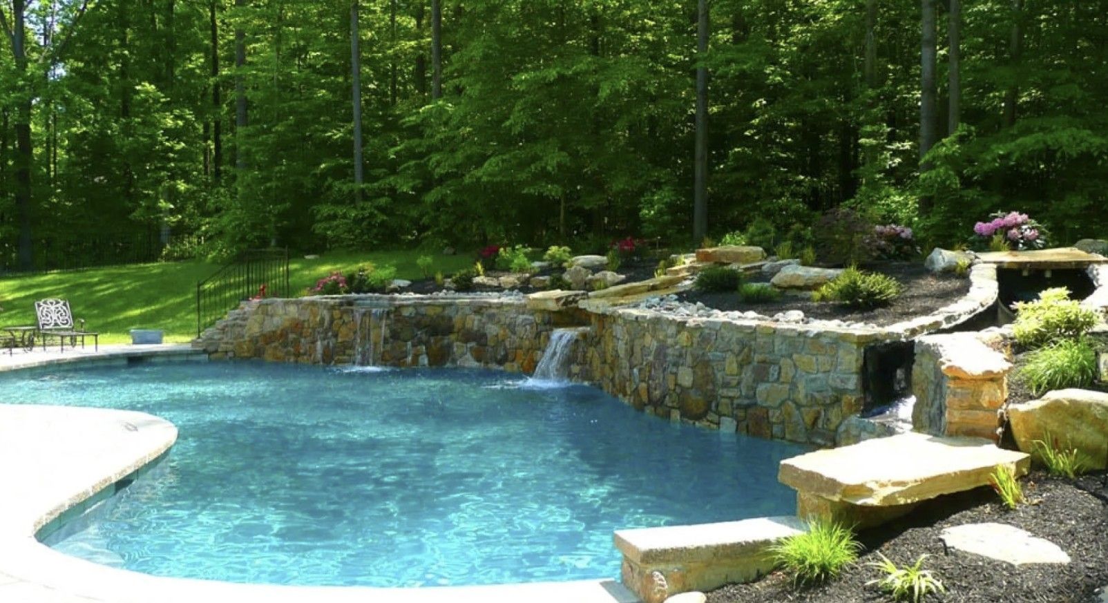 Construction of an empty, kidney-shaped swimming pool next to a lake and a white house.