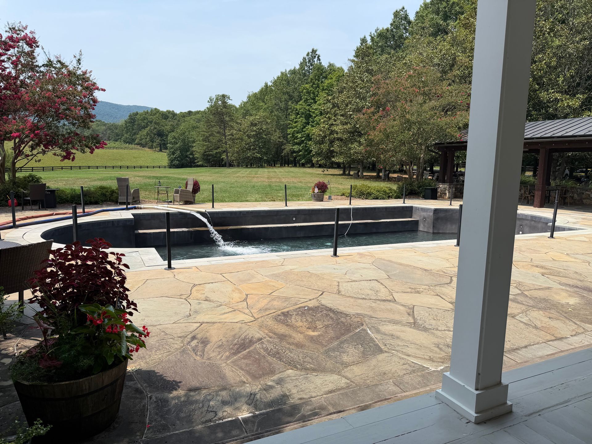 Patio with a small fountain, potted plants, and a grassy landscape beyond