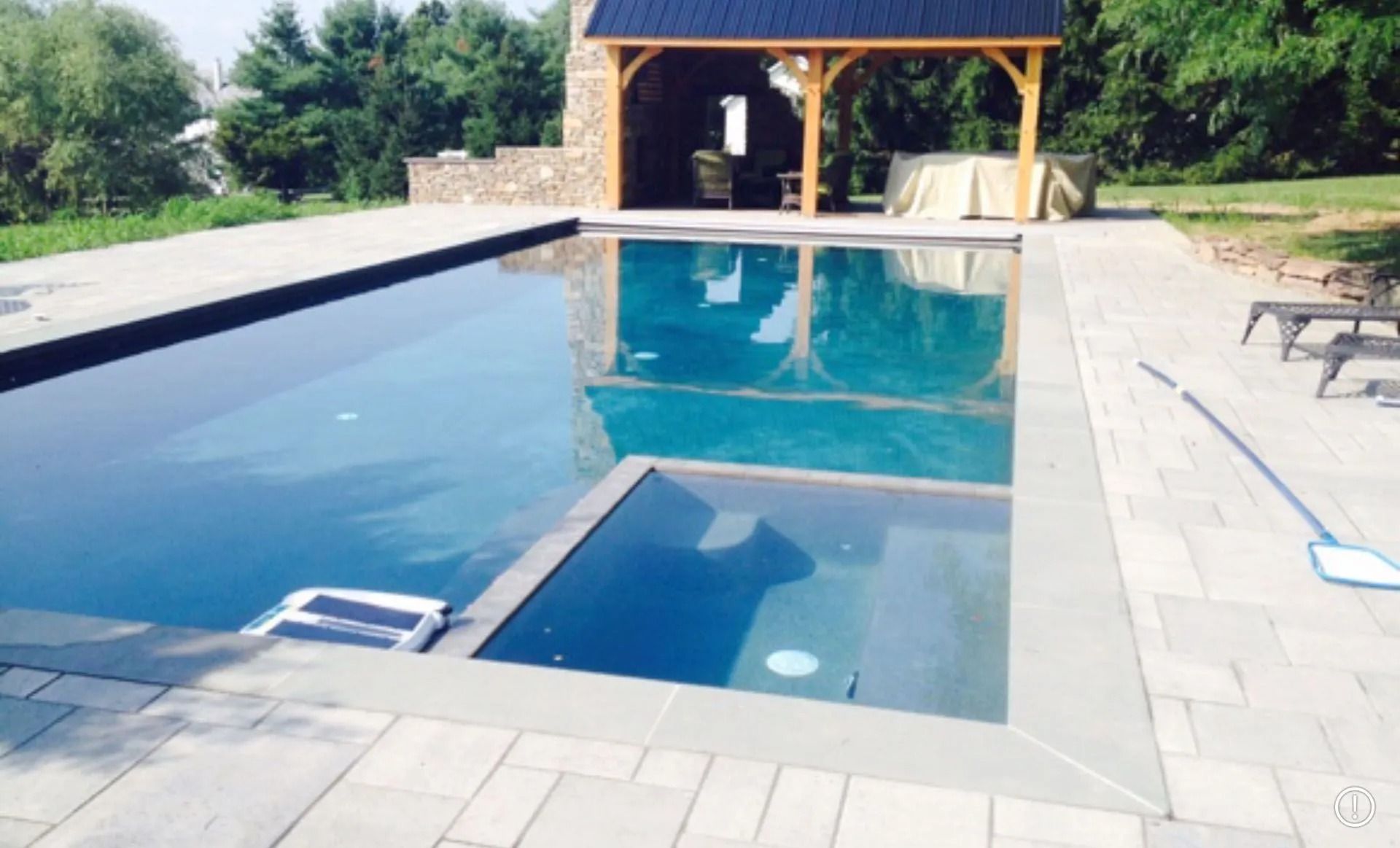 Rectangular pool with attached spa and wooden gazebo on a paved patio.