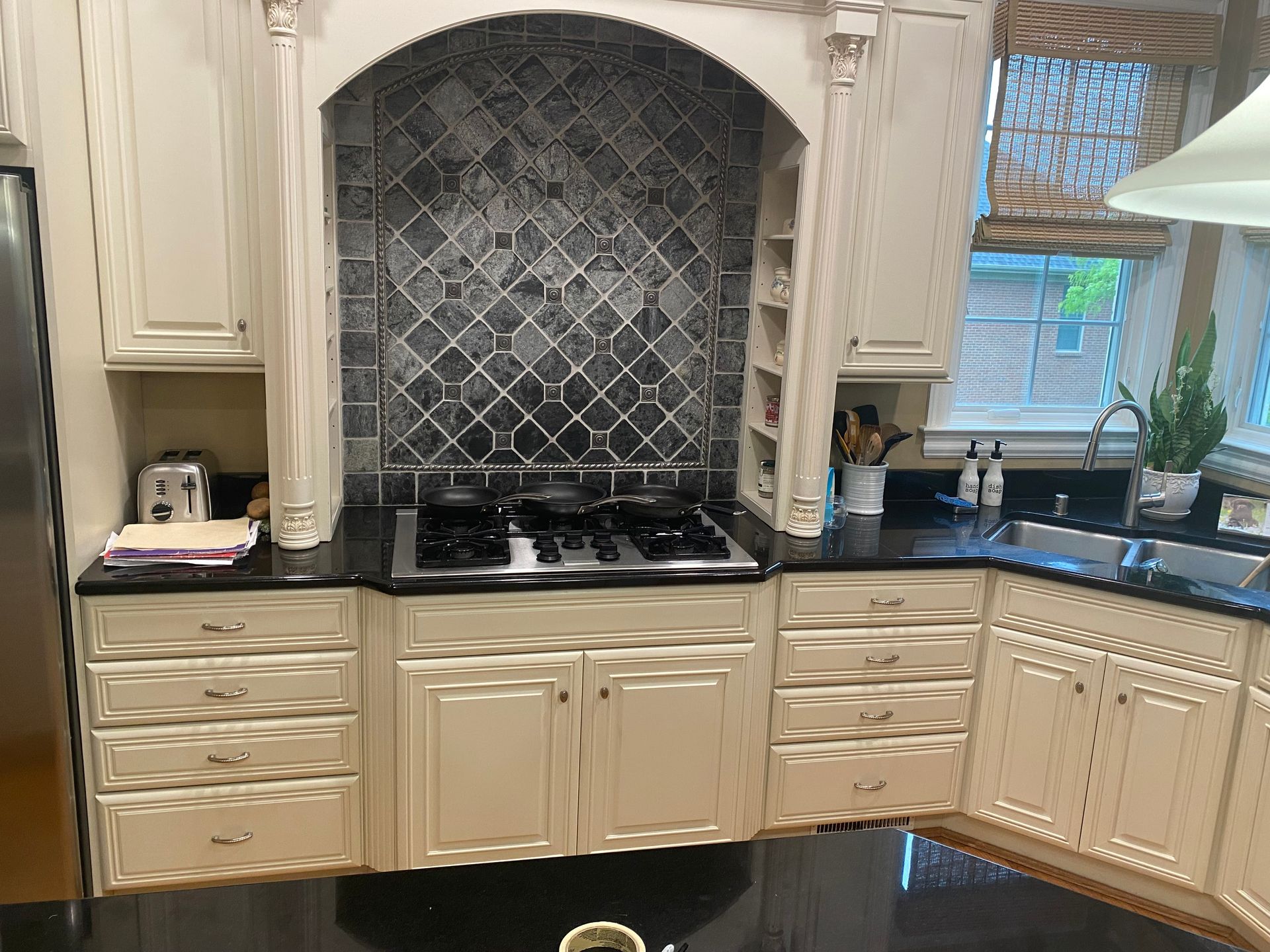 Elegant kitchen with cream cabinets, black countertop, and tiled backsplash under an arched alcove