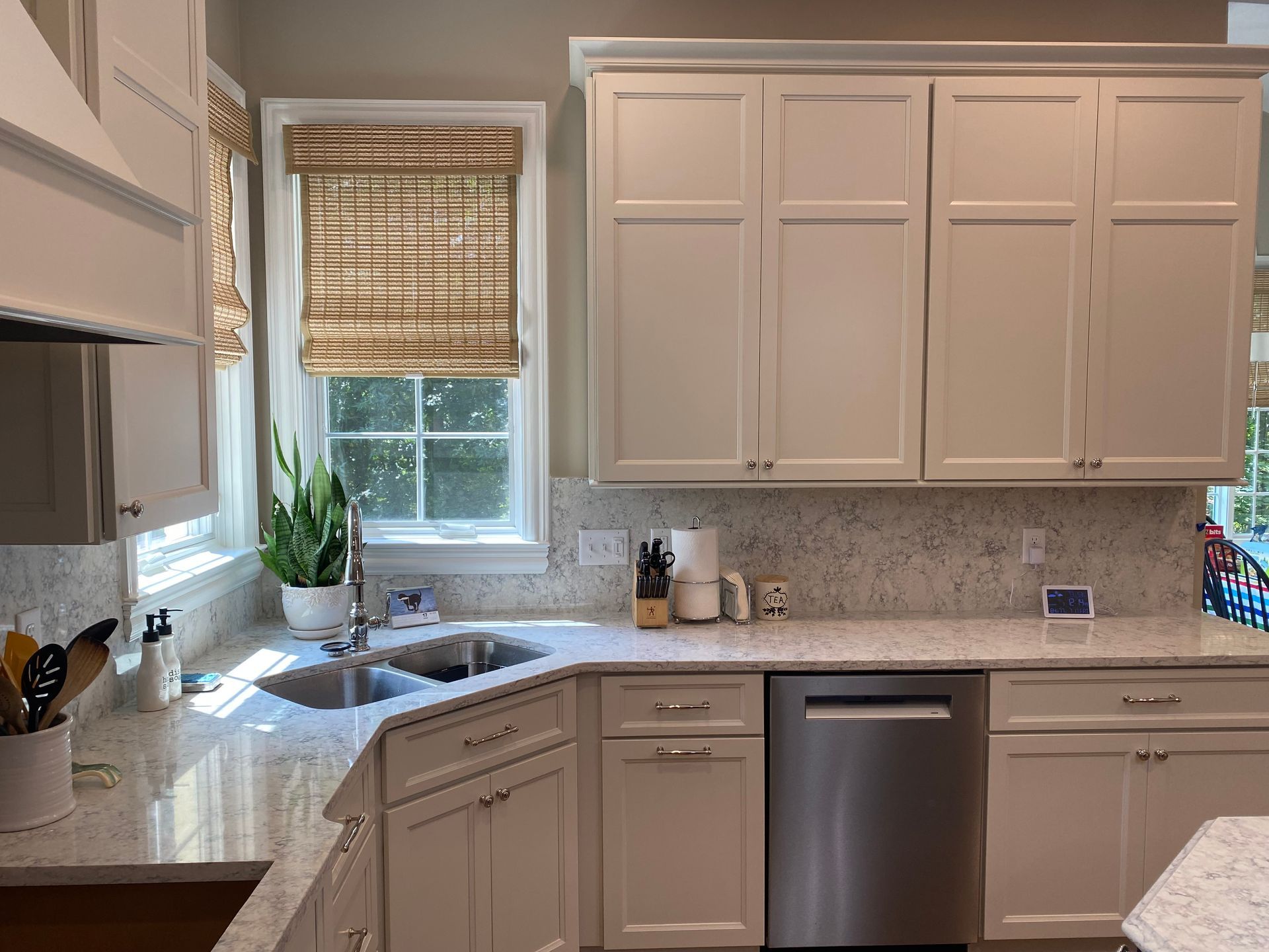 Bright kitchen with white cabinets, gray countertops, stainless dishwasher, and a sink by a window with blinds.