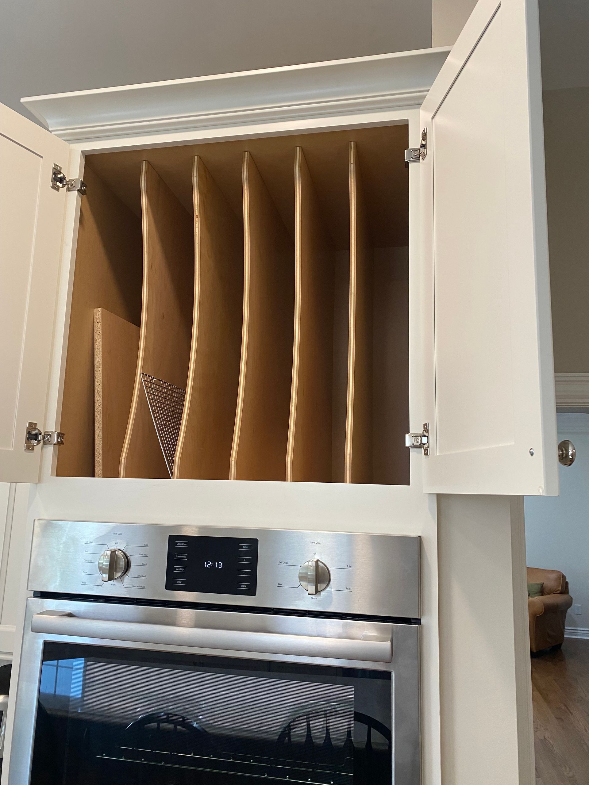 Kitchen cabinet above a stainless steel oven, with dividers inside and white doors open