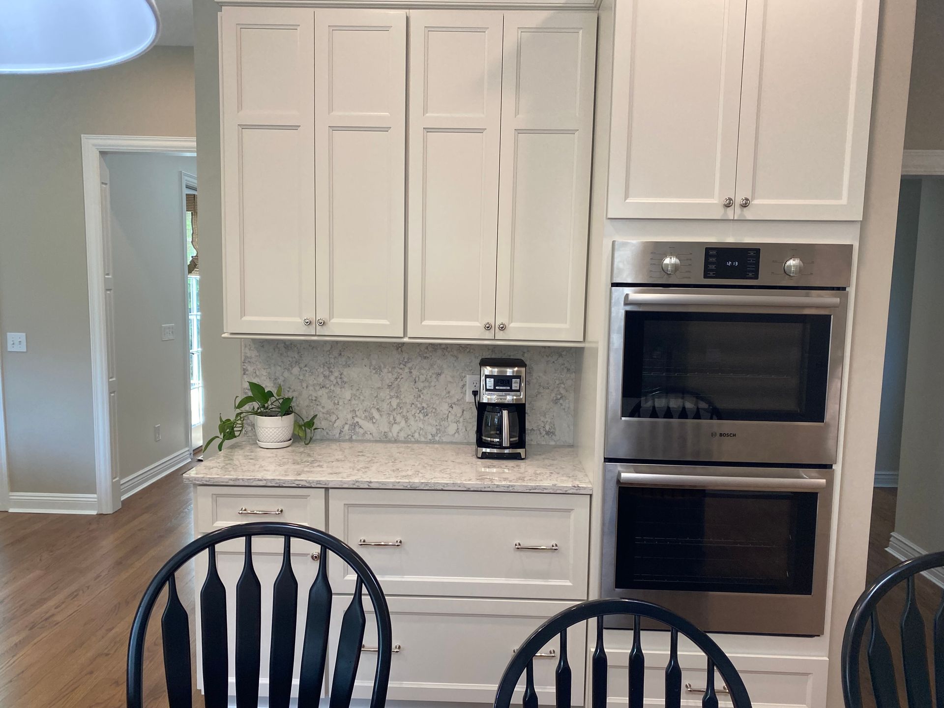Bright kitchen with white cabinets, built-in oven, coffee maker, and black dining chairs in the foreground
