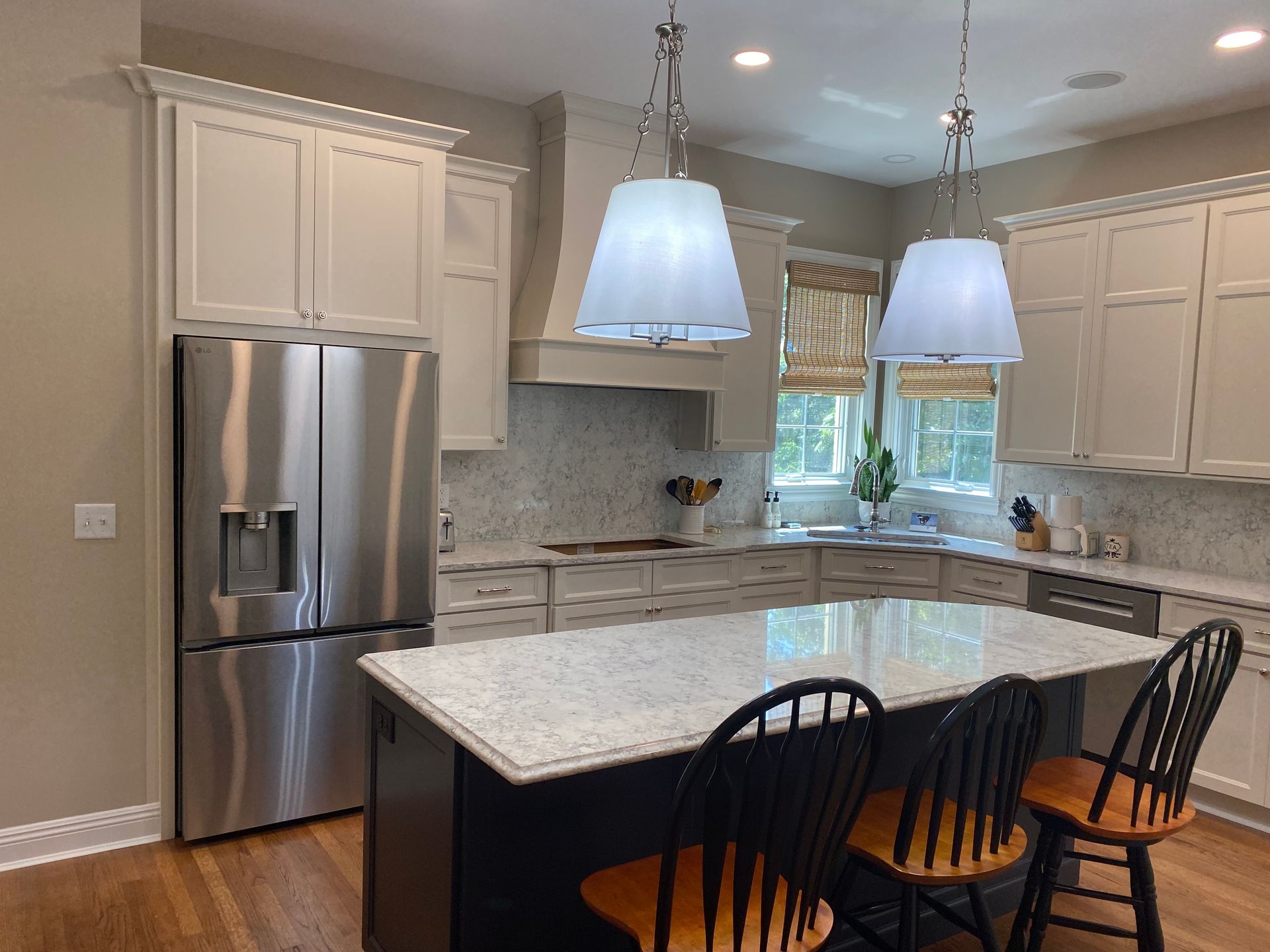 Modern kitchen with stainless steel fridge, marble island, white cabinets, and two pendant lights