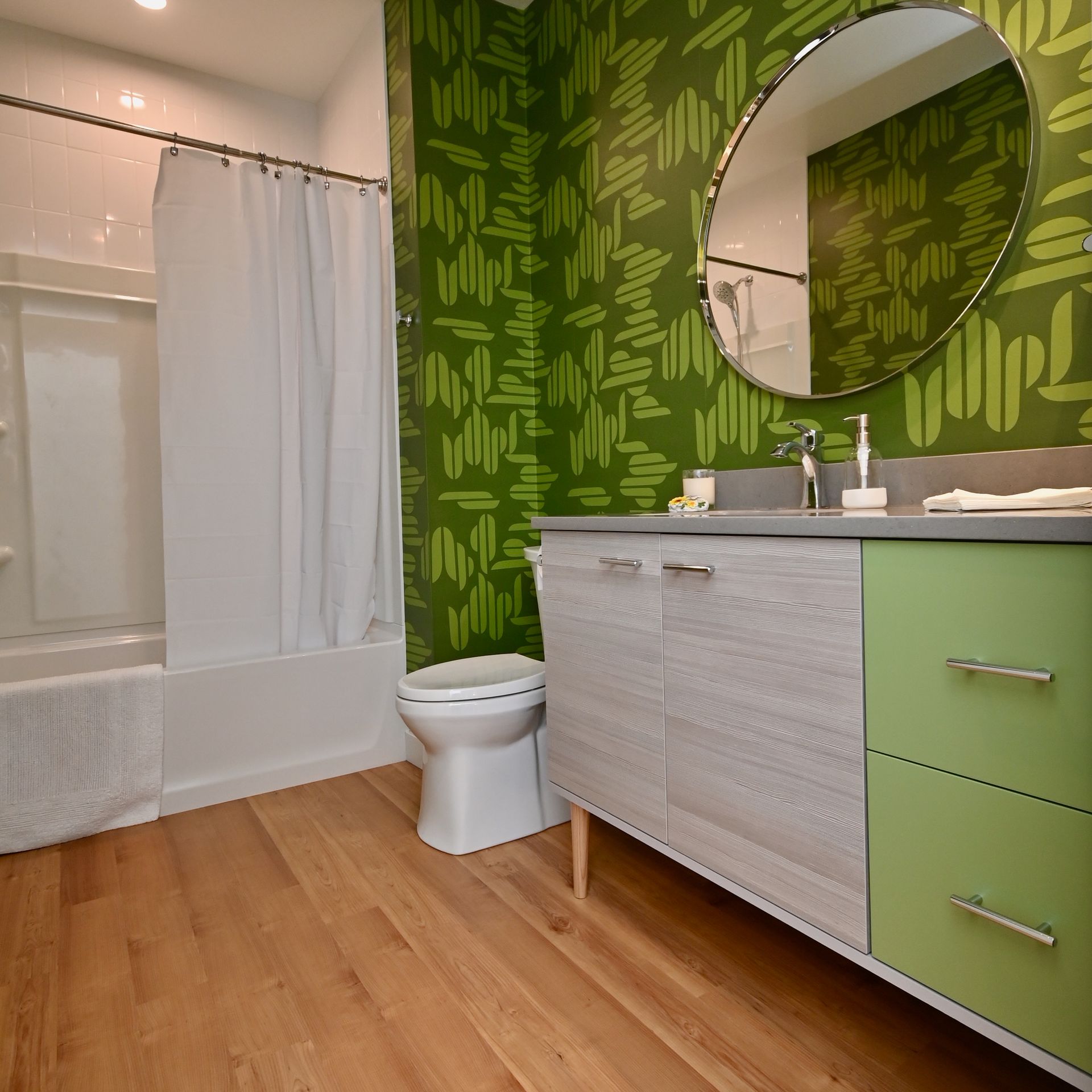 Bathroom with green patterned wallpaper, light wood floor, white fixtures, and a green vanity.