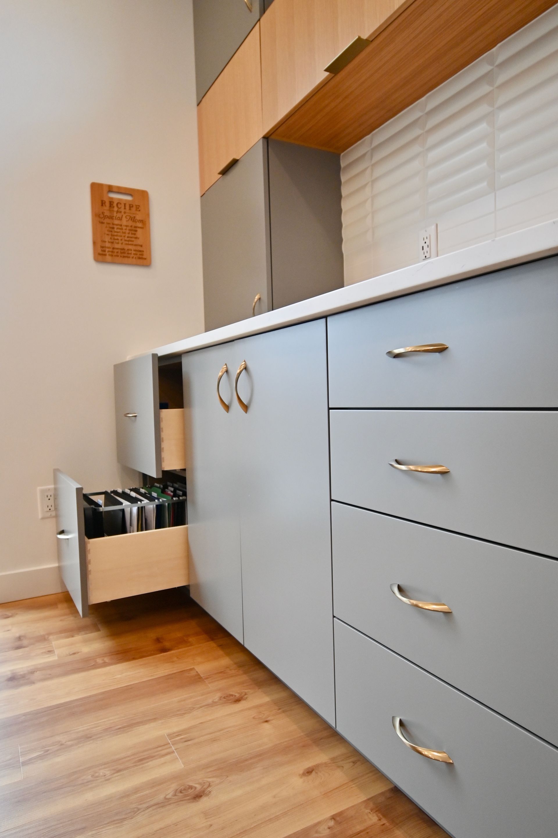 Gray kitchen cabinets with gold hardware and a spice drawer open, near a white countertop.
