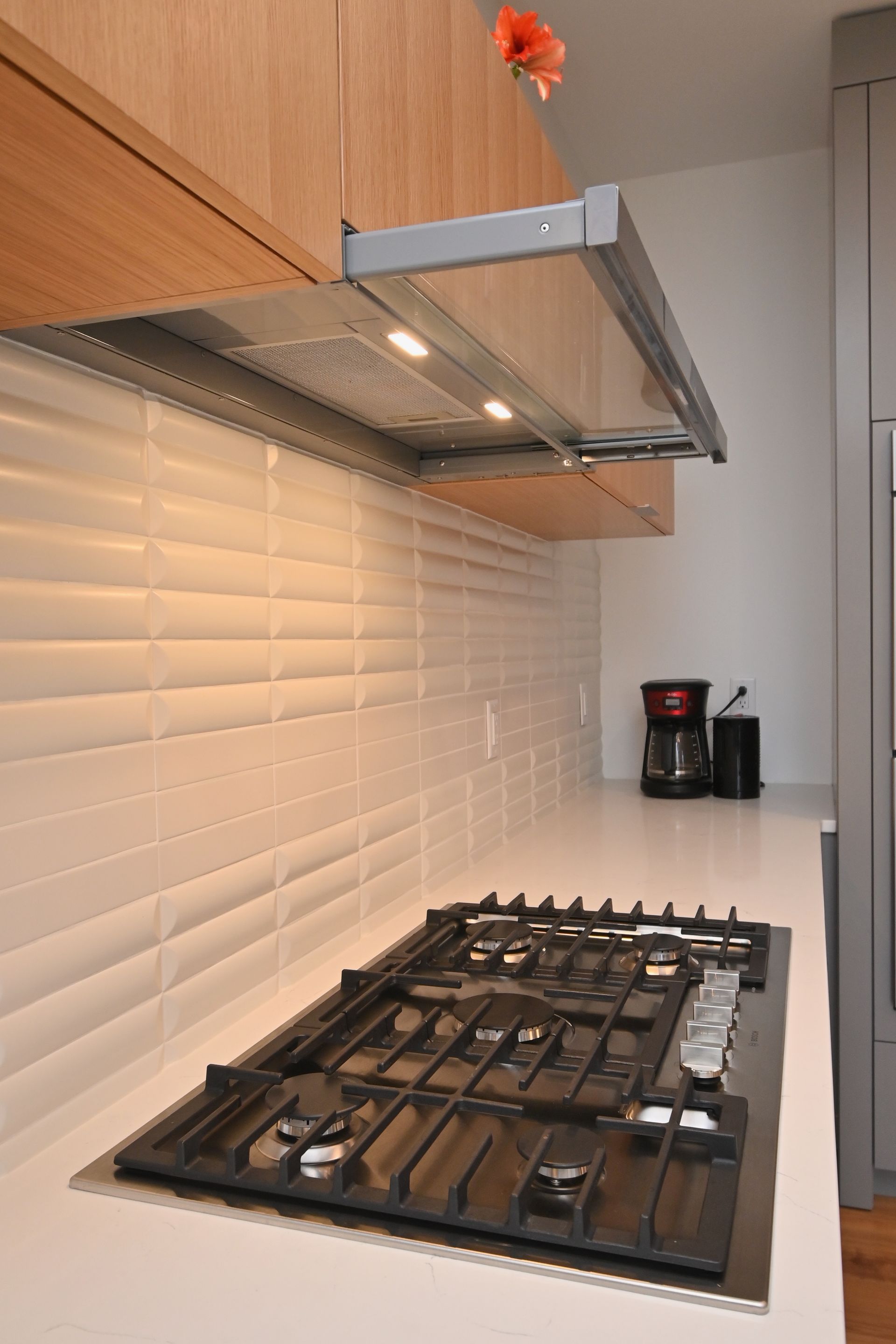 Modern kitchen with stovetop, range hood, and textured white backsplash.