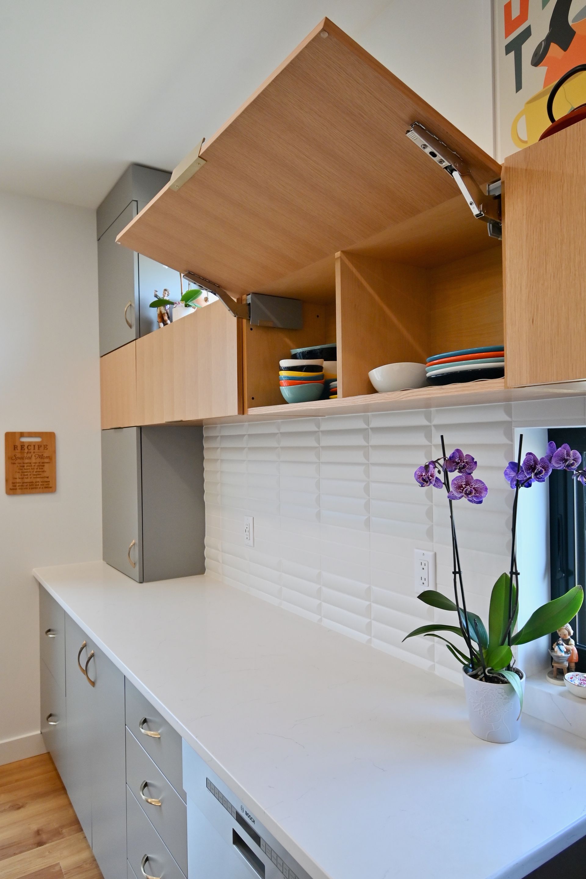Modern kitchen with open, light-wood cabinets above white countertop and backsplash, orchid, and gray lower cabinets.