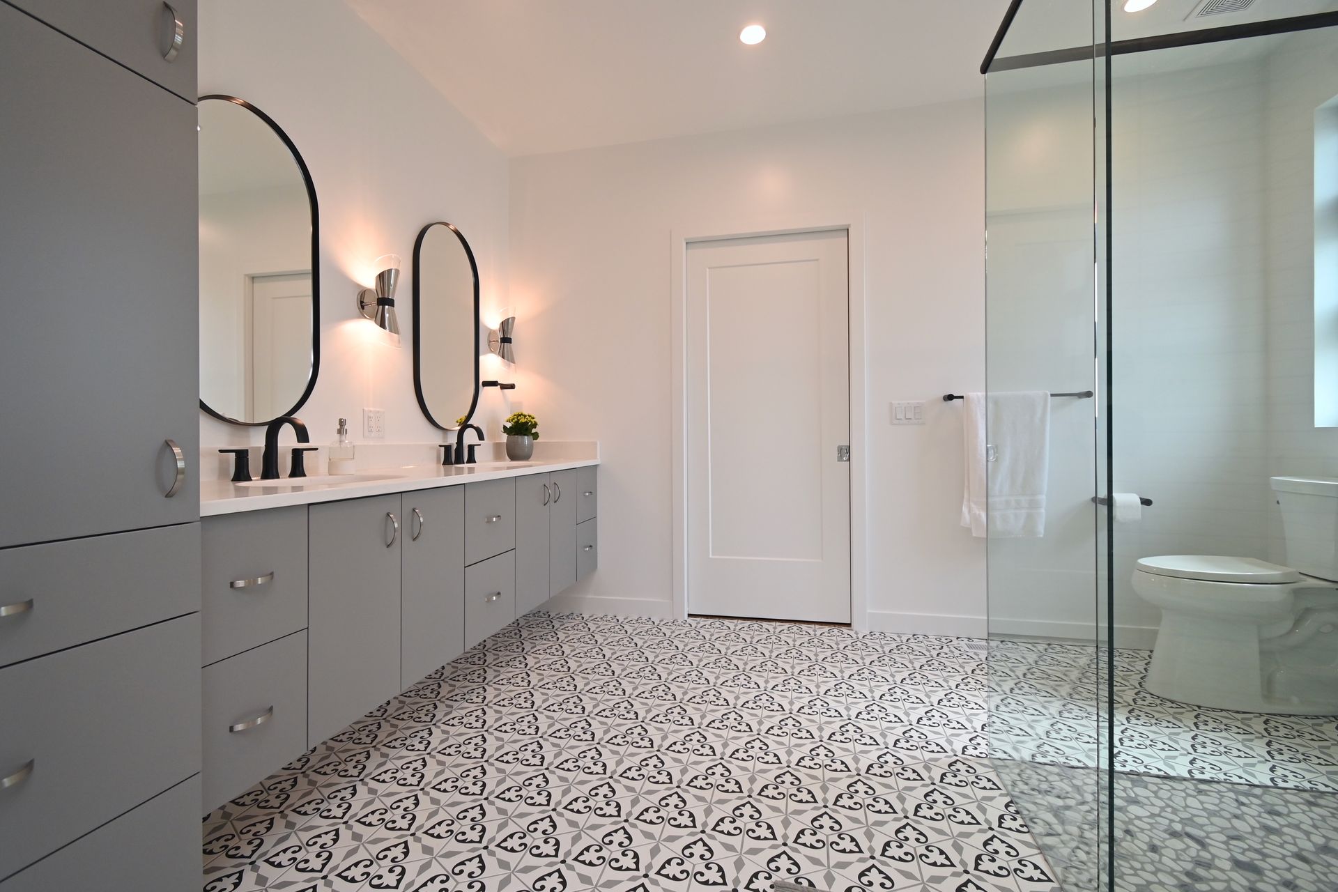 Modern bathroom with gray cabinets, patterned floor tiles, and a glass shower.