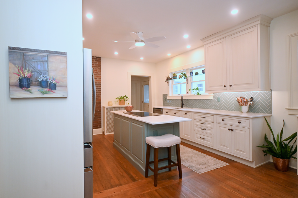 Kitchen with white cabinets, blue island, wood floors, and plants.
