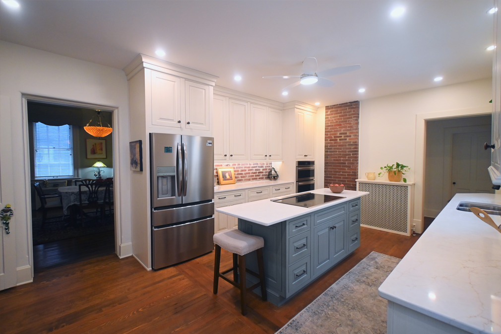Kitchen with blue island, stainless steel refrigerator, white cabinets, and exposed brick.