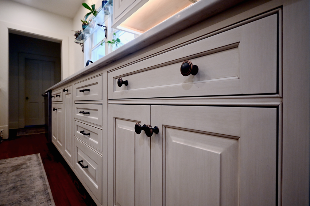 Cream-colored kitchen cabinets with dark knobs. A countertop and a doorway are also visible.