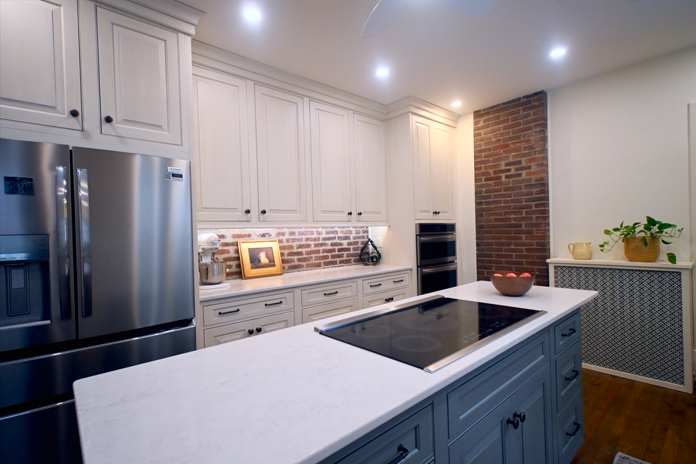 Modern kitchen with white and gray cabinets, stainless steel appliances, brick accent wall, and island with cooktop.