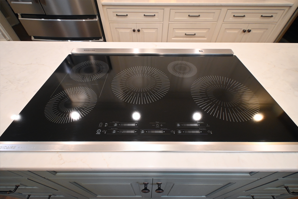 Black glass induction cooktop with illuminated burners set into a white countertop.