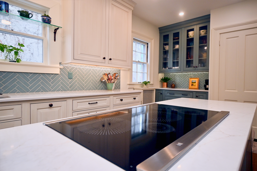 Modern kitchen with white cabinets, blue backsplash, and a black cooktop on the island.