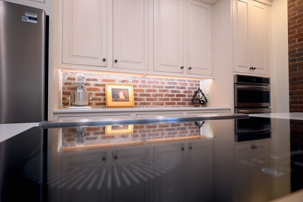 Kitchen with white cabinets, brick backsplash, stainless steel appliances, and a reflective island.