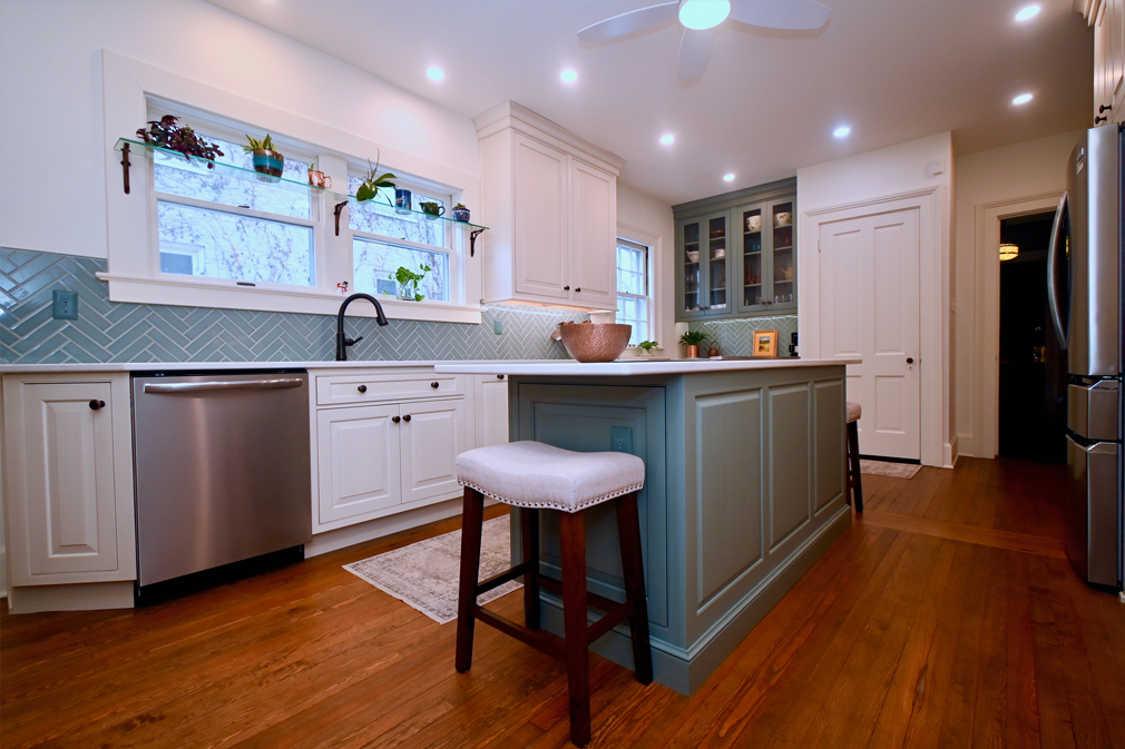 Kitchen with white cabinets, blue backsplash, green island, stainless steel appliances, and wooden floors.