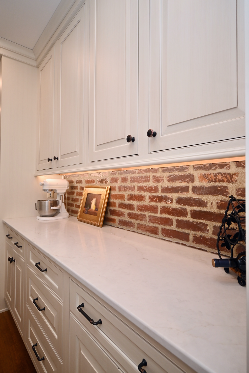 White cabinets above and below a countertop, with brick backsplash and a mixer.
