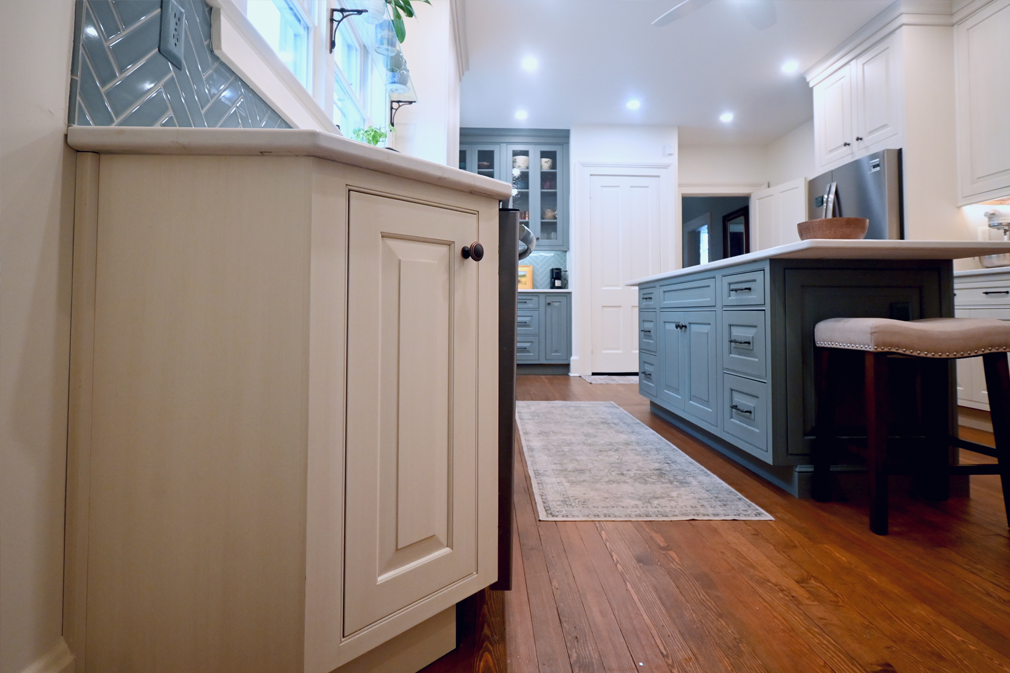 Kitchen with blue and white cabinets, marble countertop, wooden floor, and a rug.